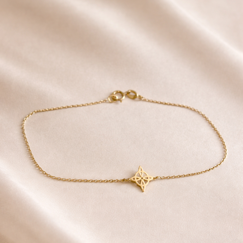 Pulsera delicada de oro amarillo 18k con diseño de nudo de bruja sobre cadena fina, usada en muñeca femenina con outfit de lino en tonos beige.