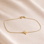 Pulsera delicada de oro amarillo 18k con diseño de nudo de bruja sobre cadena fina, usada en muñeca femenina con outfit de lino en tonos beige.