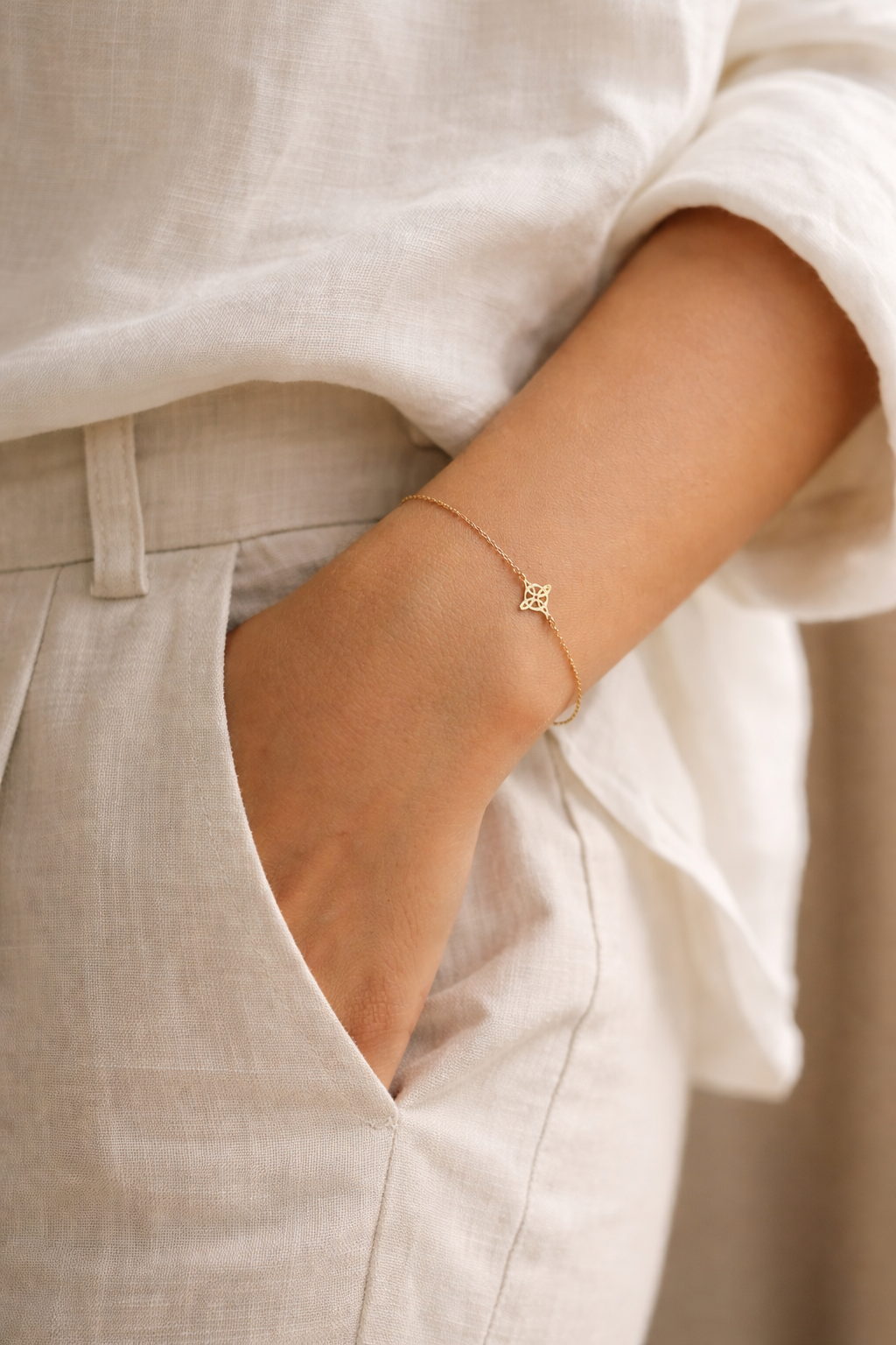 Pulsera de oro amarillo 18 quilates con símbolo nudo de bruja en cadena fina, lucida en muñeca de mujer con vestuario en tonos neutros estilo minimalista.